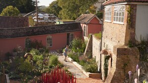 A courtyard with a brick pathway, a pink building, and a person walking. - Bishopstrow Hotel & Spa (Warminster)