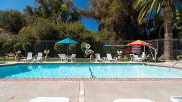 A swimming pool with lounge chairs and umbrellas, surrounded by a fence and trees.
