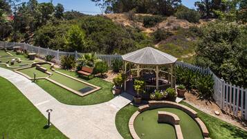A well-maintained garden with a gazebo, a putting green, and a walking path.