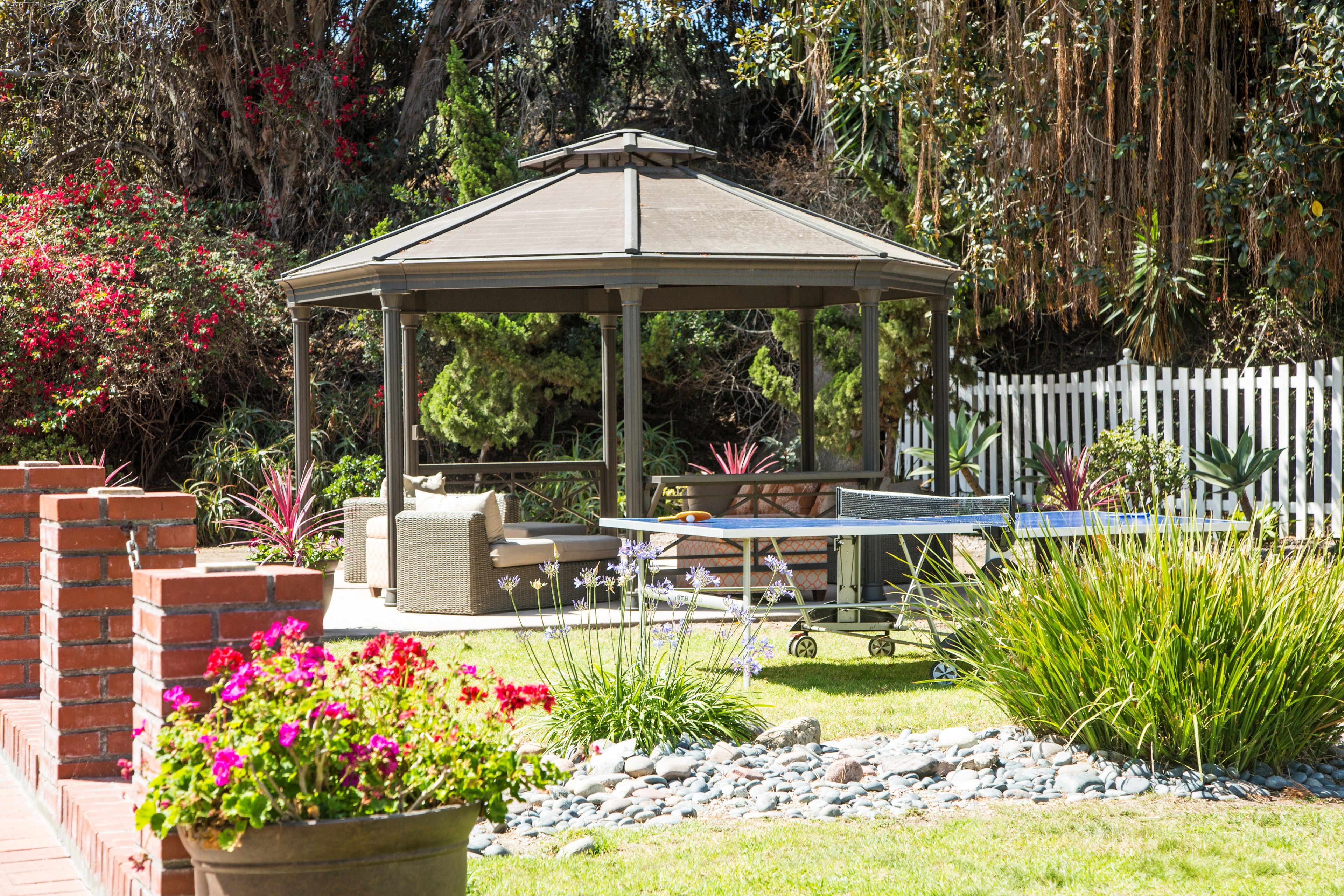 Un pabellón con una mesa y sillas, rodeado por un jardín con diversas plantas y flores.