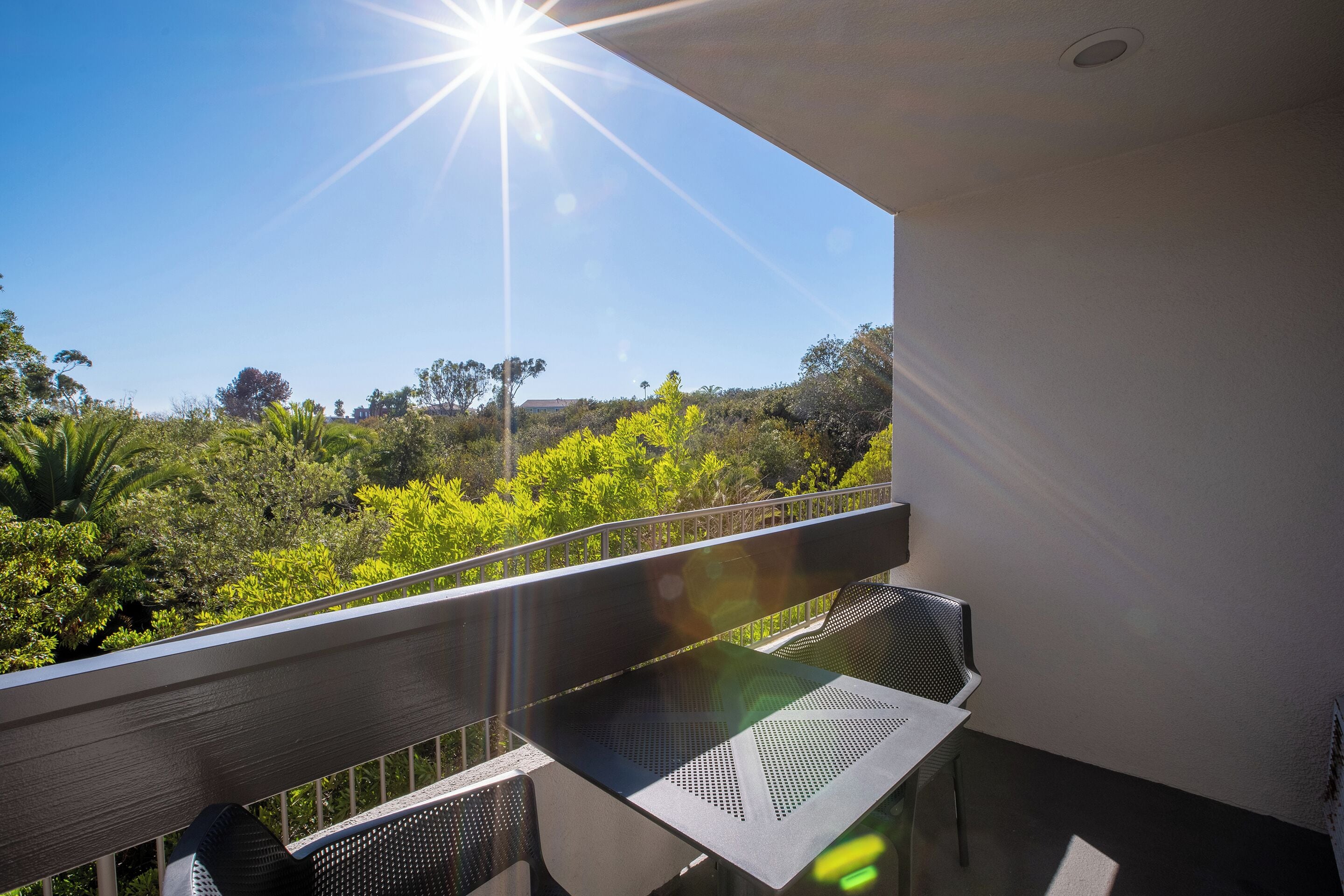 A balcony with a table and chairs, overlooking a lush green landscape.