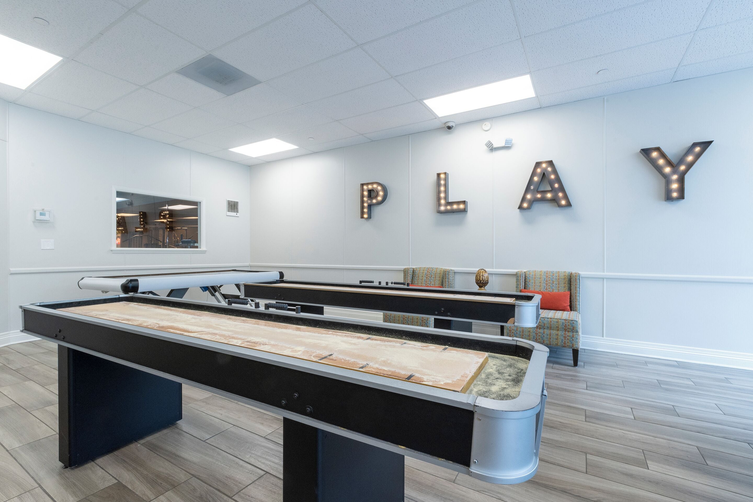 A pool table in a room with a 'PLAY' sign on the wall and a chair with a cushion.