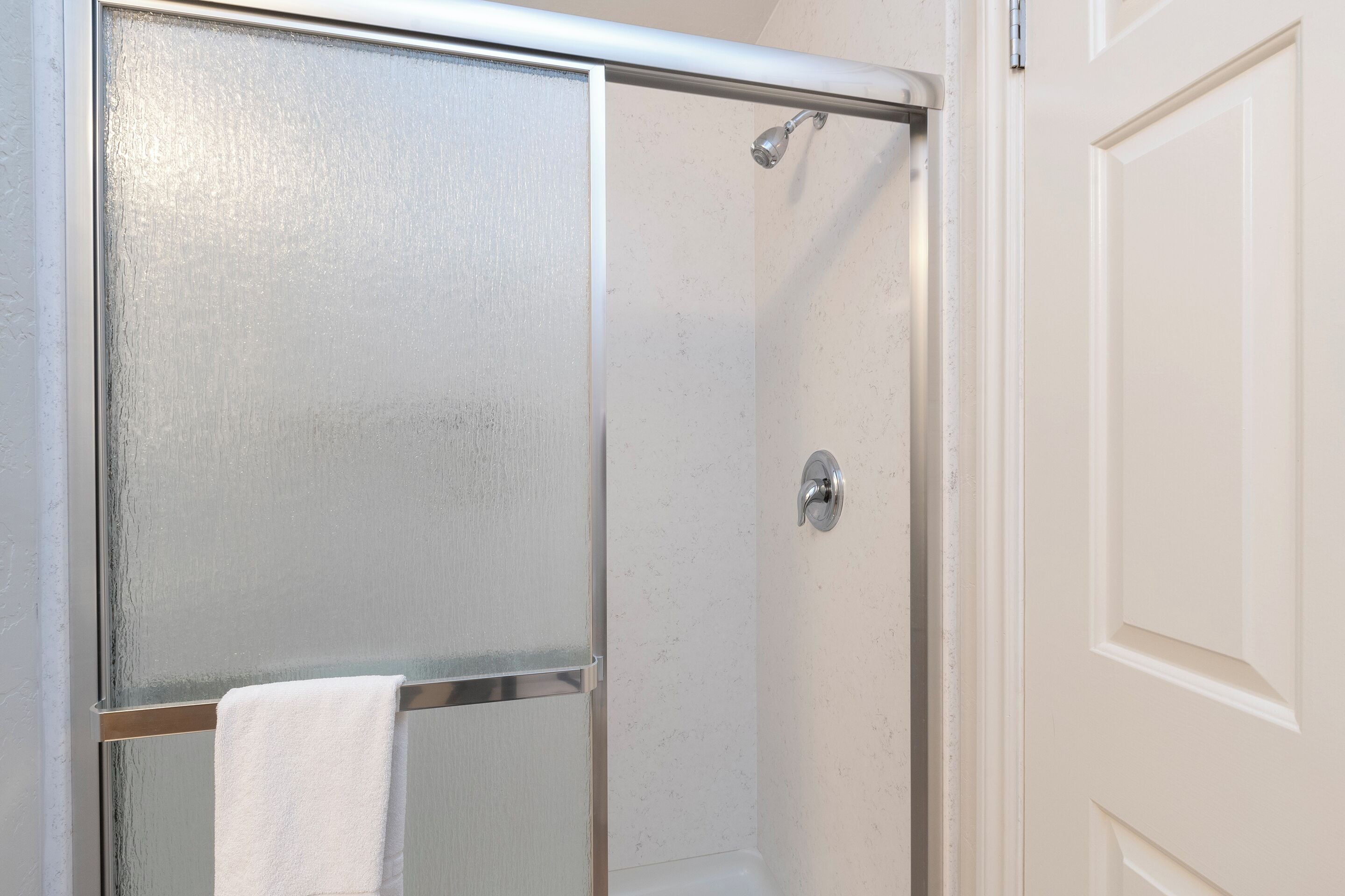 A bathroom with a glass shower door, a white towel hanging on the door, and a white door frame.