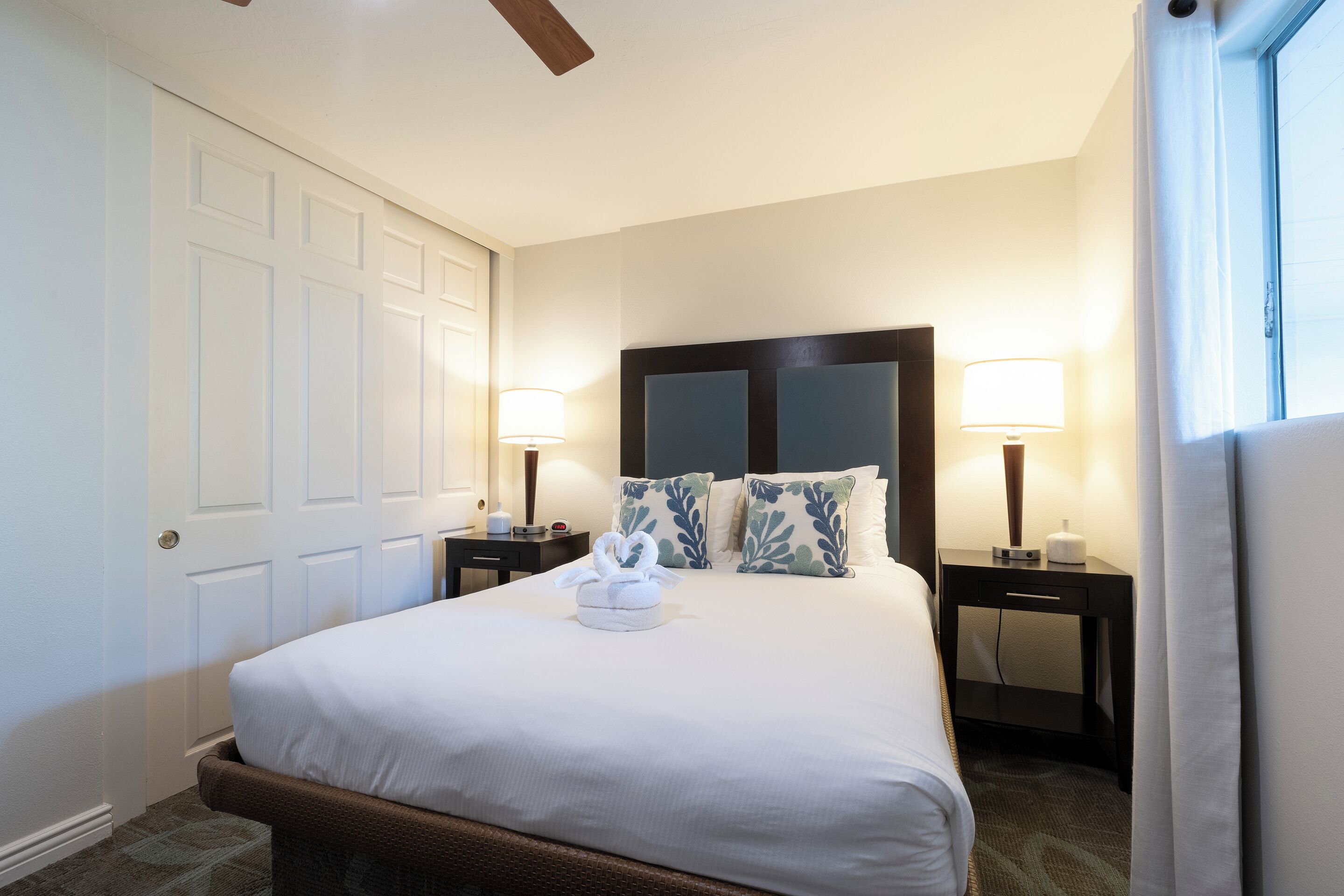 Una habitación de hotel con una cama grande, dos mesitas de noche con lámparas, un cabecero y una puerta.
