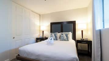 Una habitación de hotel con una cama grande, dos mesitas de noche con lámparas, un cabecero y una puerta.