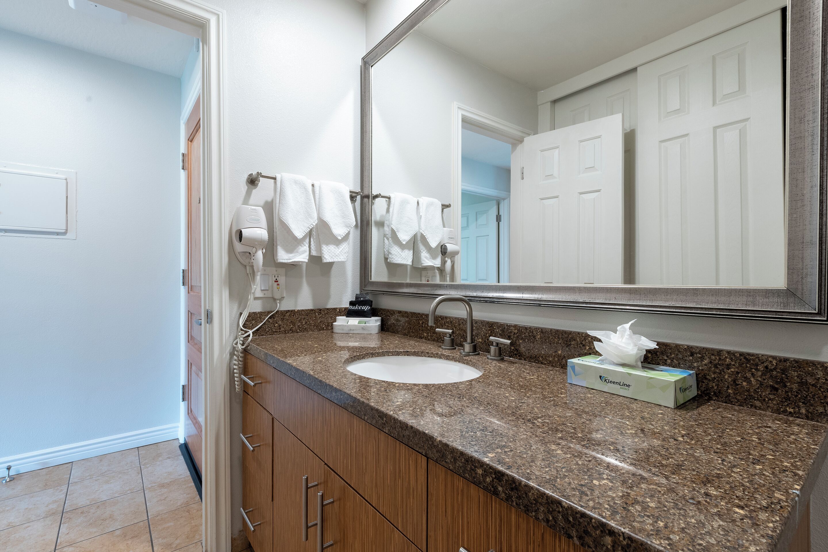 Une salle de bain avec un comptoir en granit, un lavabo blanc, un miroir et un porte-serviettes.
