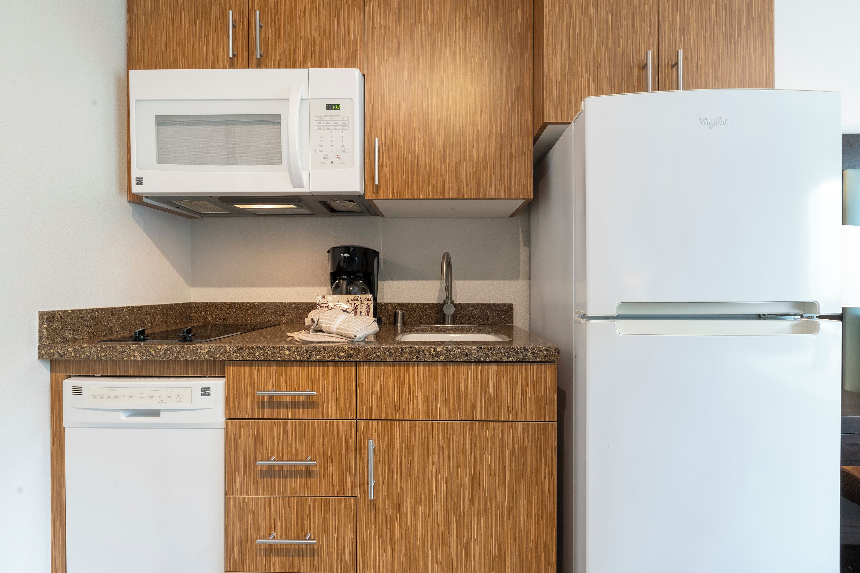 A compact kitchen with wooden cabinets, a white microwave, a coffee maker, and a dishwasher.