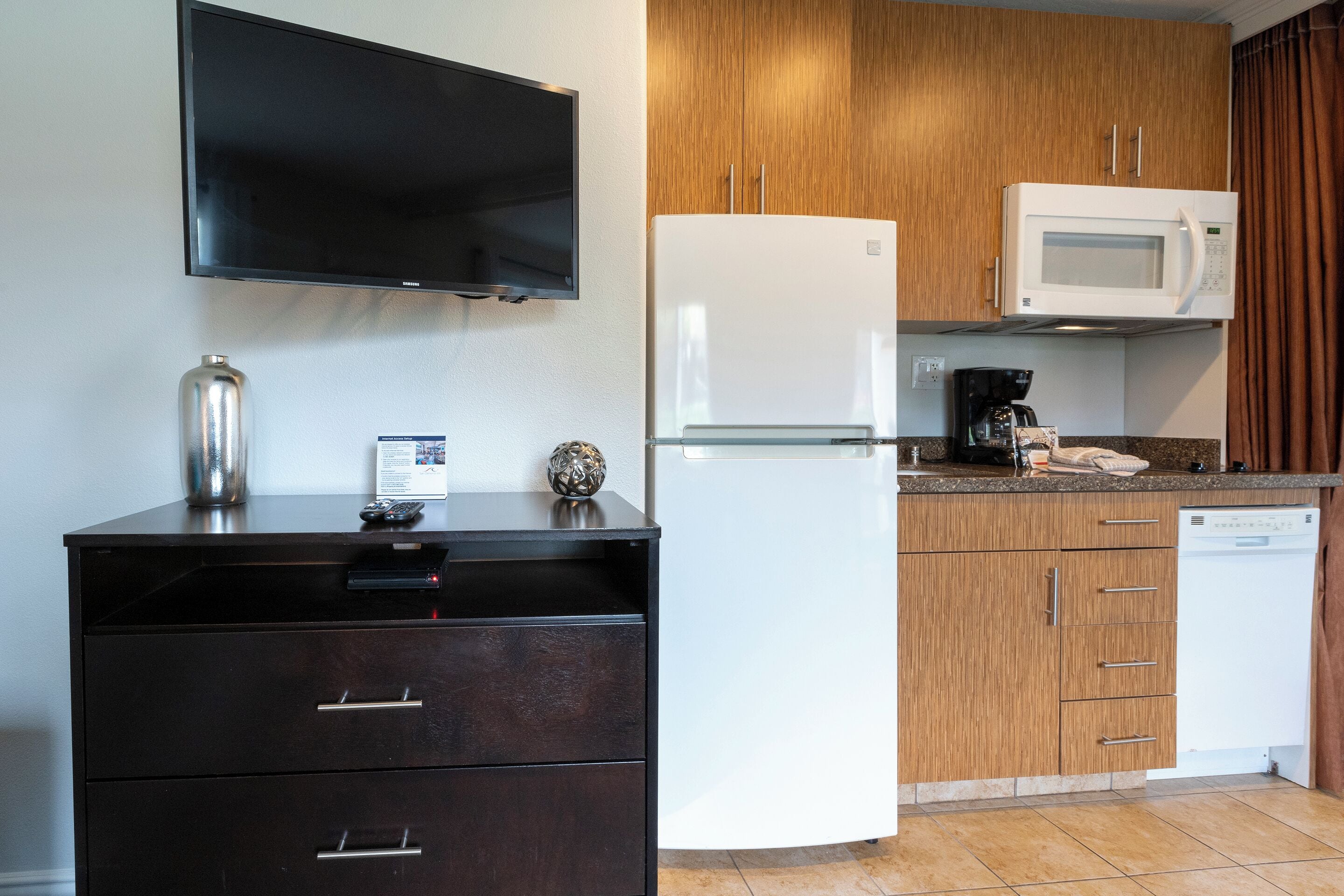 A compact kitchen with a flat-screen TV, a refrigerator, microwave, and a coffee maker.