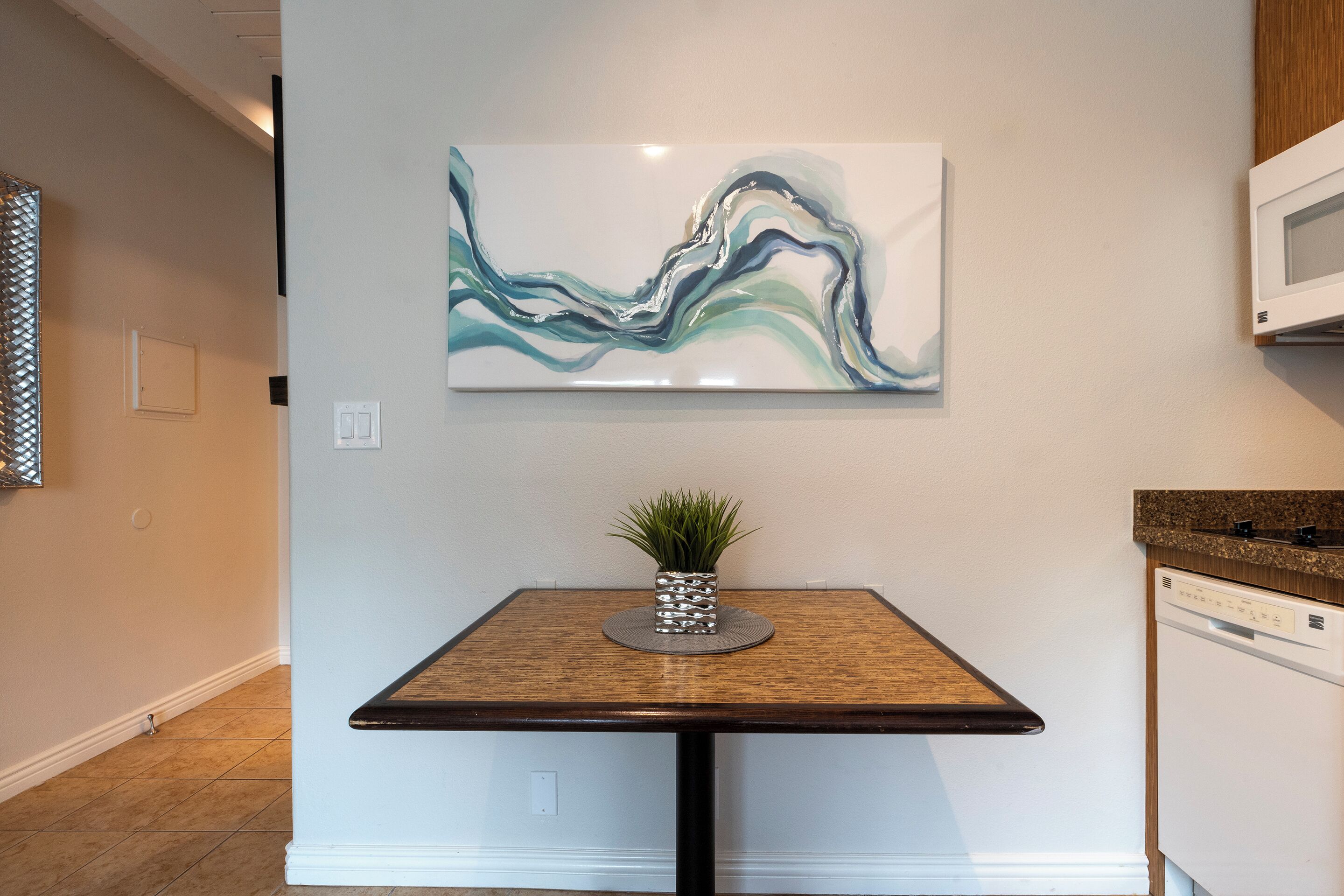 A modern kitchen with a wooden table, a potted plant, and a wall-mounted abstract painting.