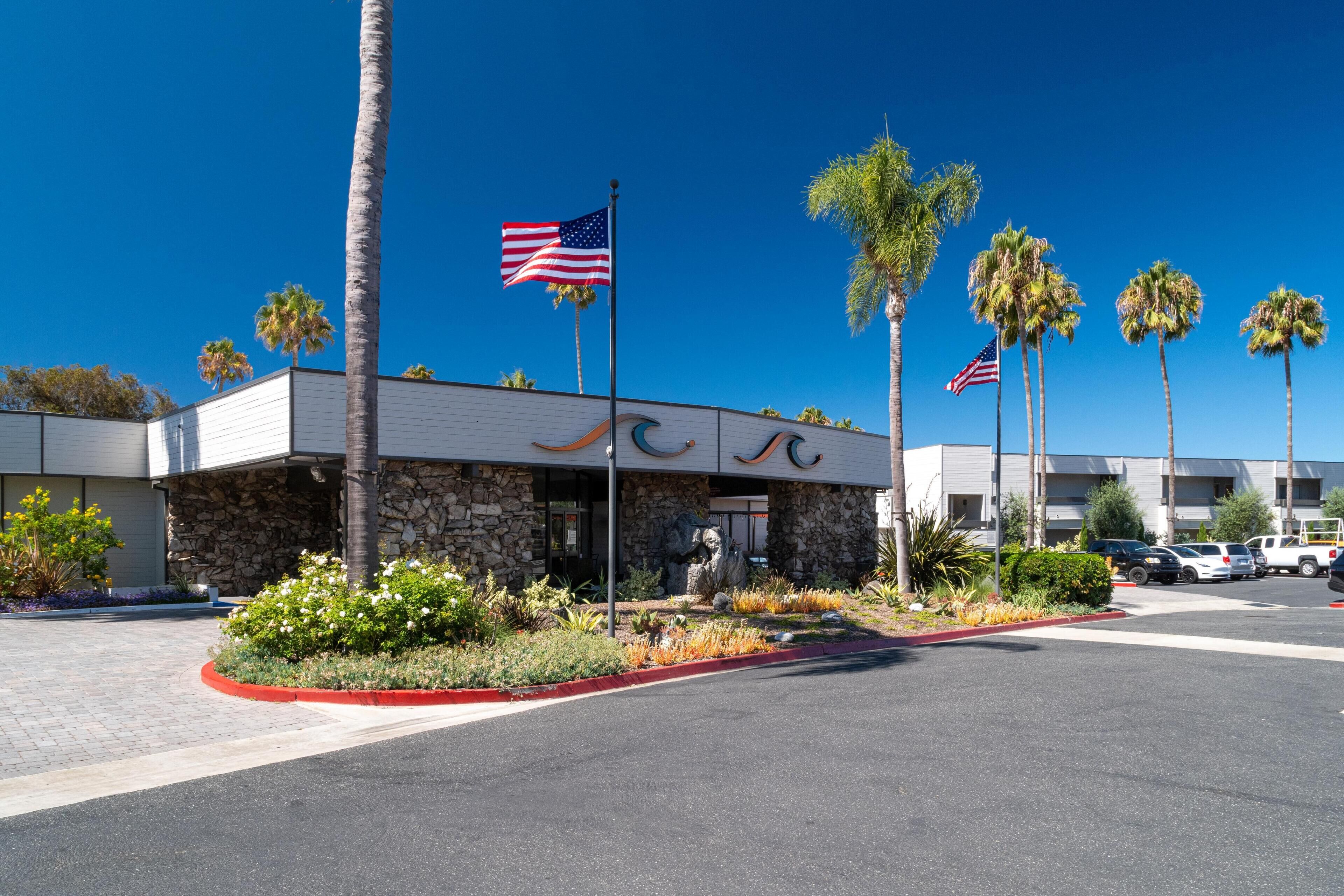 A hotel with a stone facade, palm trees, and American flags.