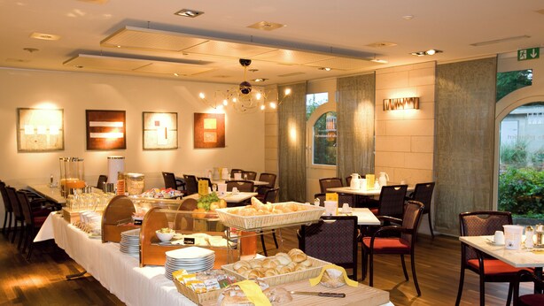 A hotel dining area with a buffet setup, including bread, pastries, and beverages.