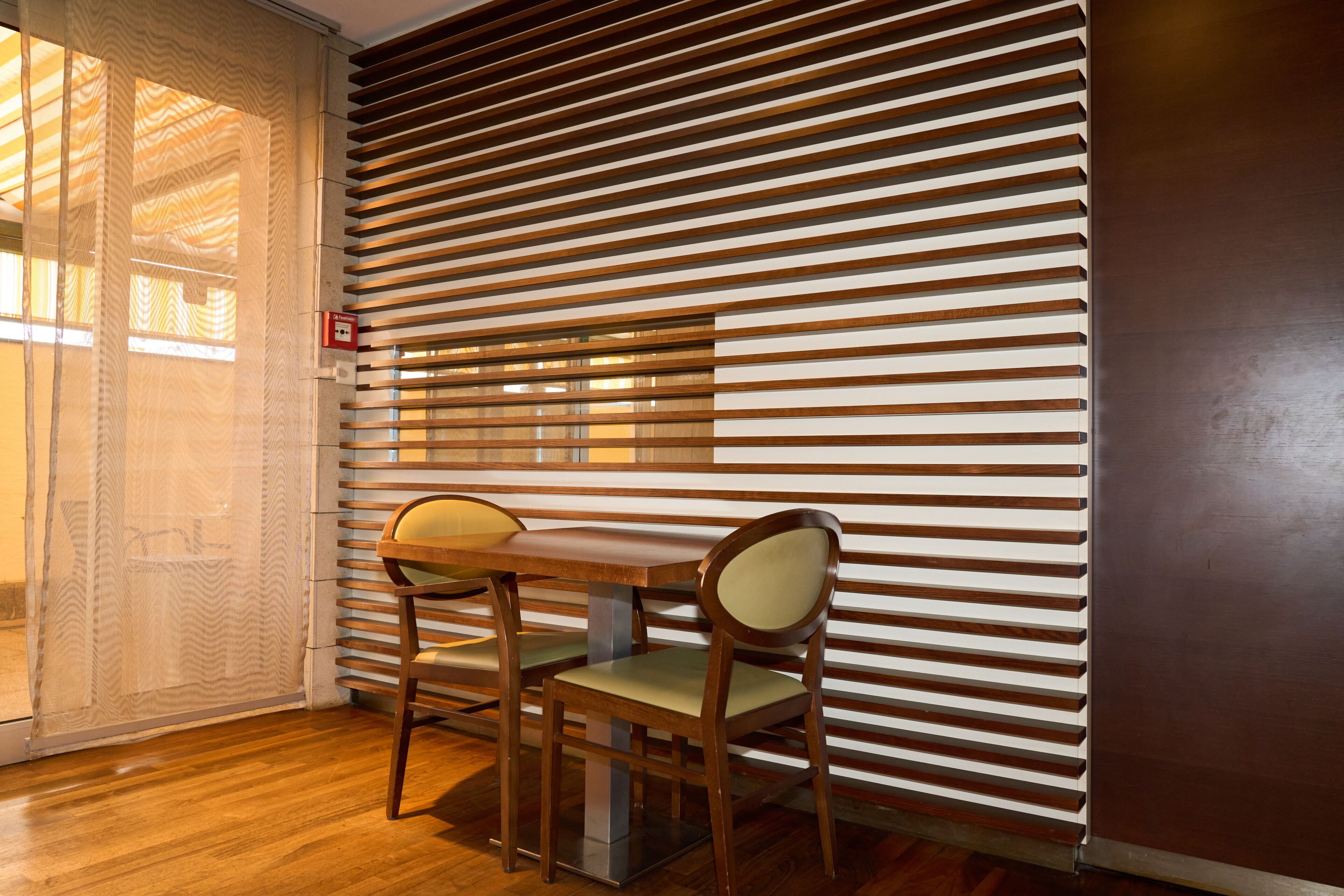 A room with a wooden floor, a table with two chairs, and a wall with horizontal slats.