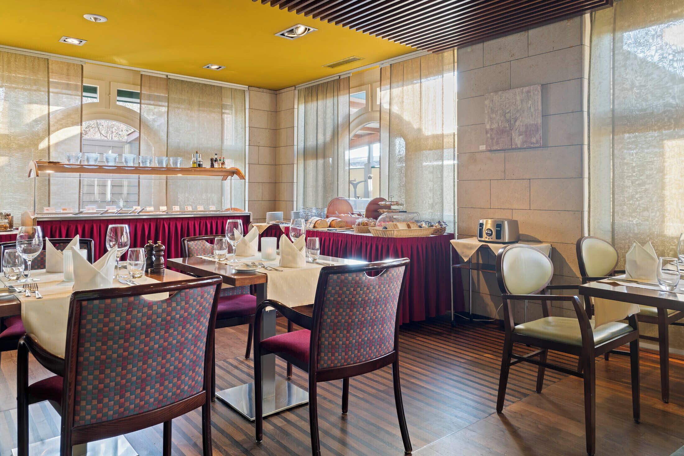 A dining area with tables set for a meal, chairs, and a buffet counter.
