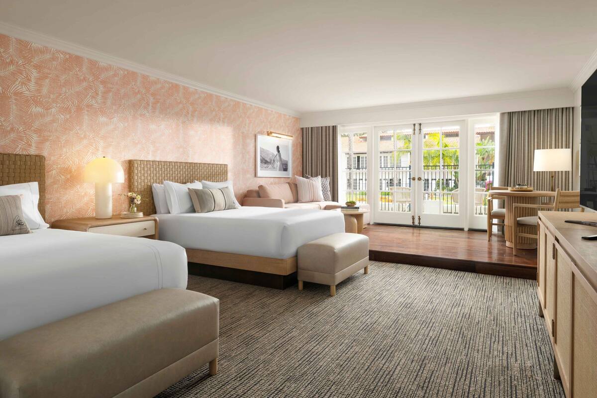 A hotel room with two beds, a desk, and a view of the outdoors.