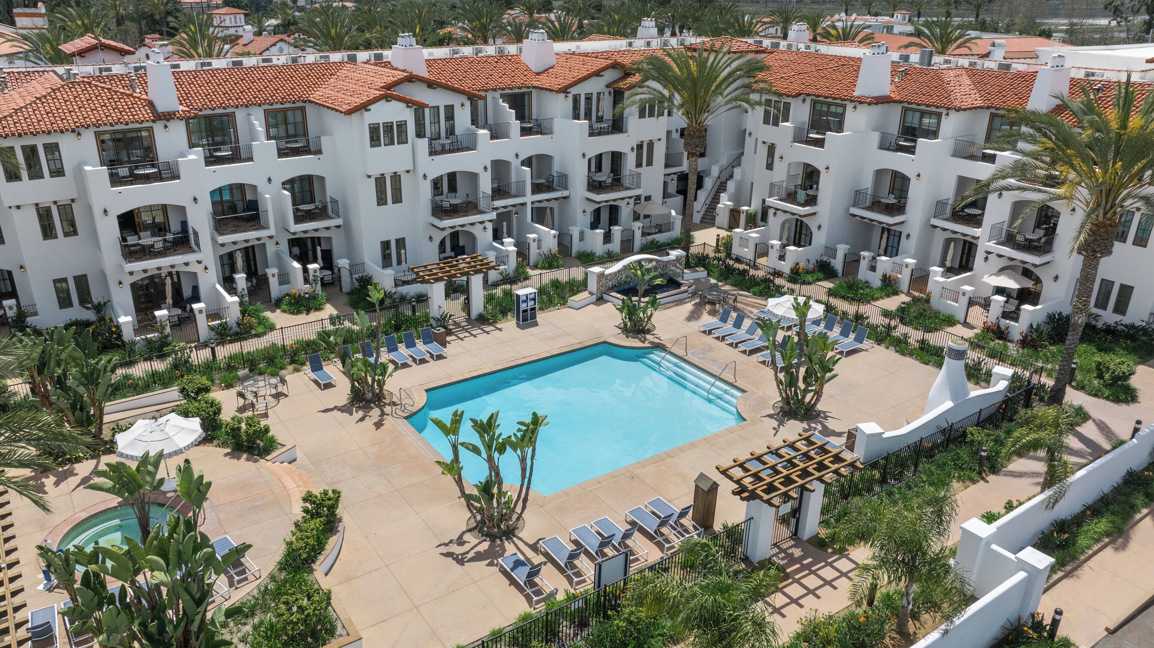 A resort with a central swimming pool surrounded by lounge chairs and palm trees.