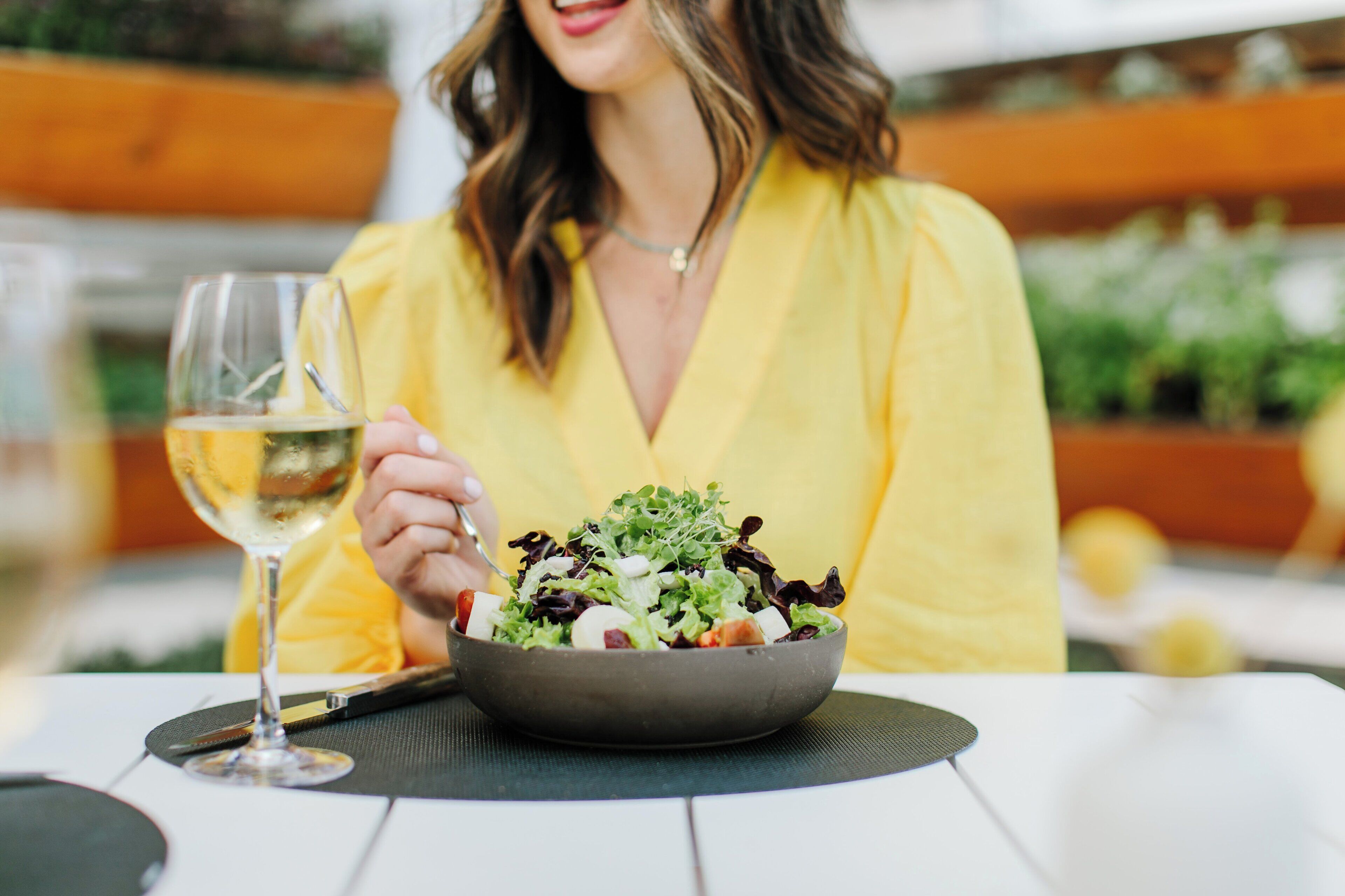 A person sitting at a table with a bowl of salad and a glass of white wine.
