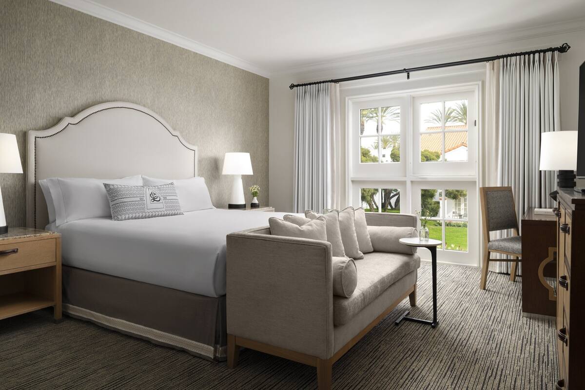 A hotel room with a large bed, a sofa, a desk, and a view of the outdoors.