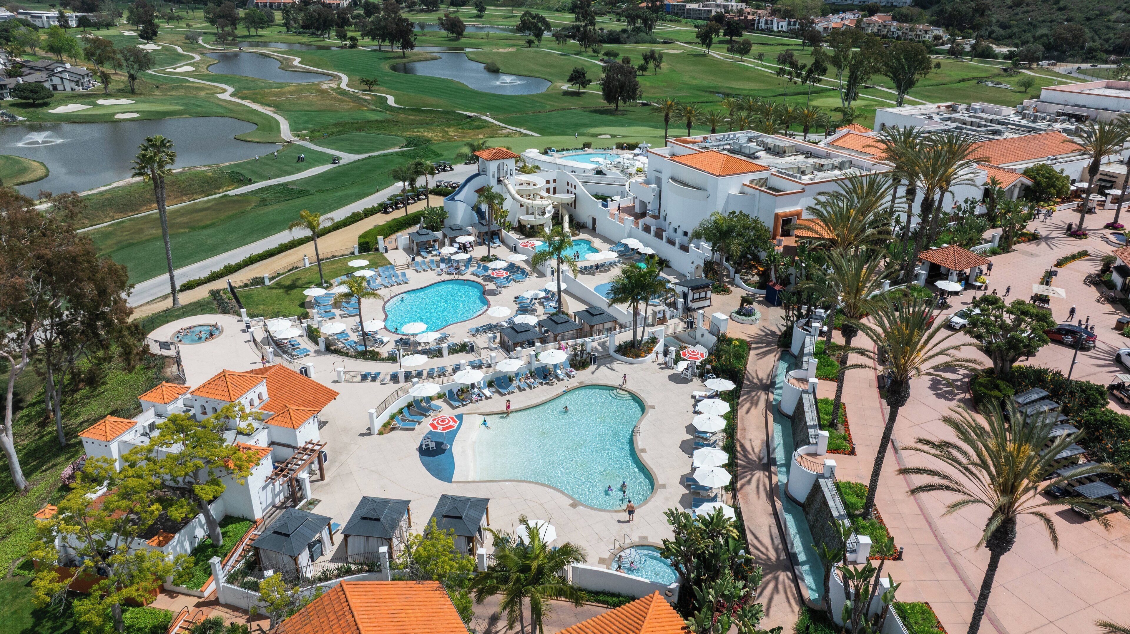Un complexe hôtelier doté de plusieurs piscines, d’un parcours de golf et d’un grand bâtiment comprenant un espace piscine sur le toit.