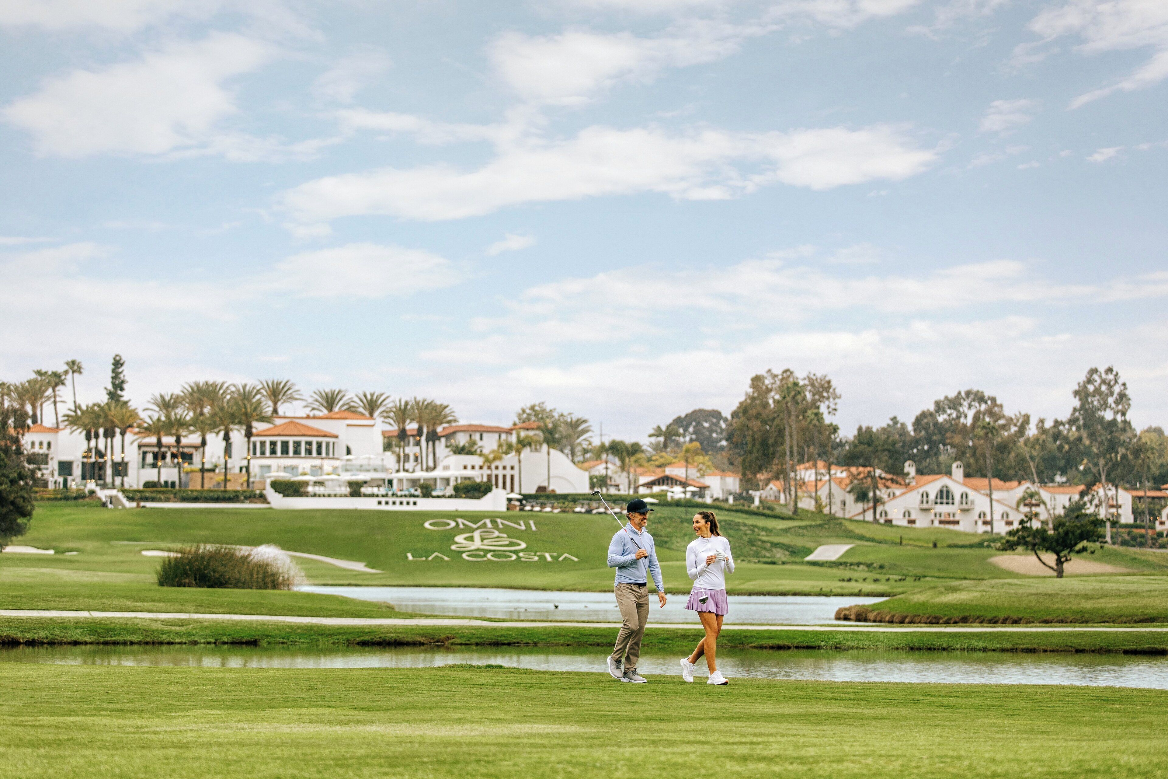 A golf course with a pond, palm trees, and a building with "OMNI LA COSTA" written on the grass.