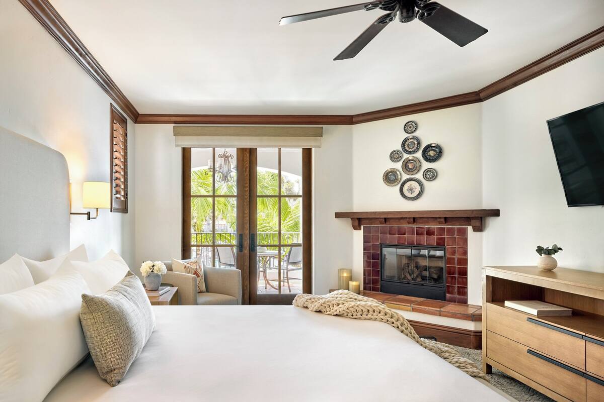A hotel room with a large bed, a fireplace, a ceiling fan, and a view of the outdoors.