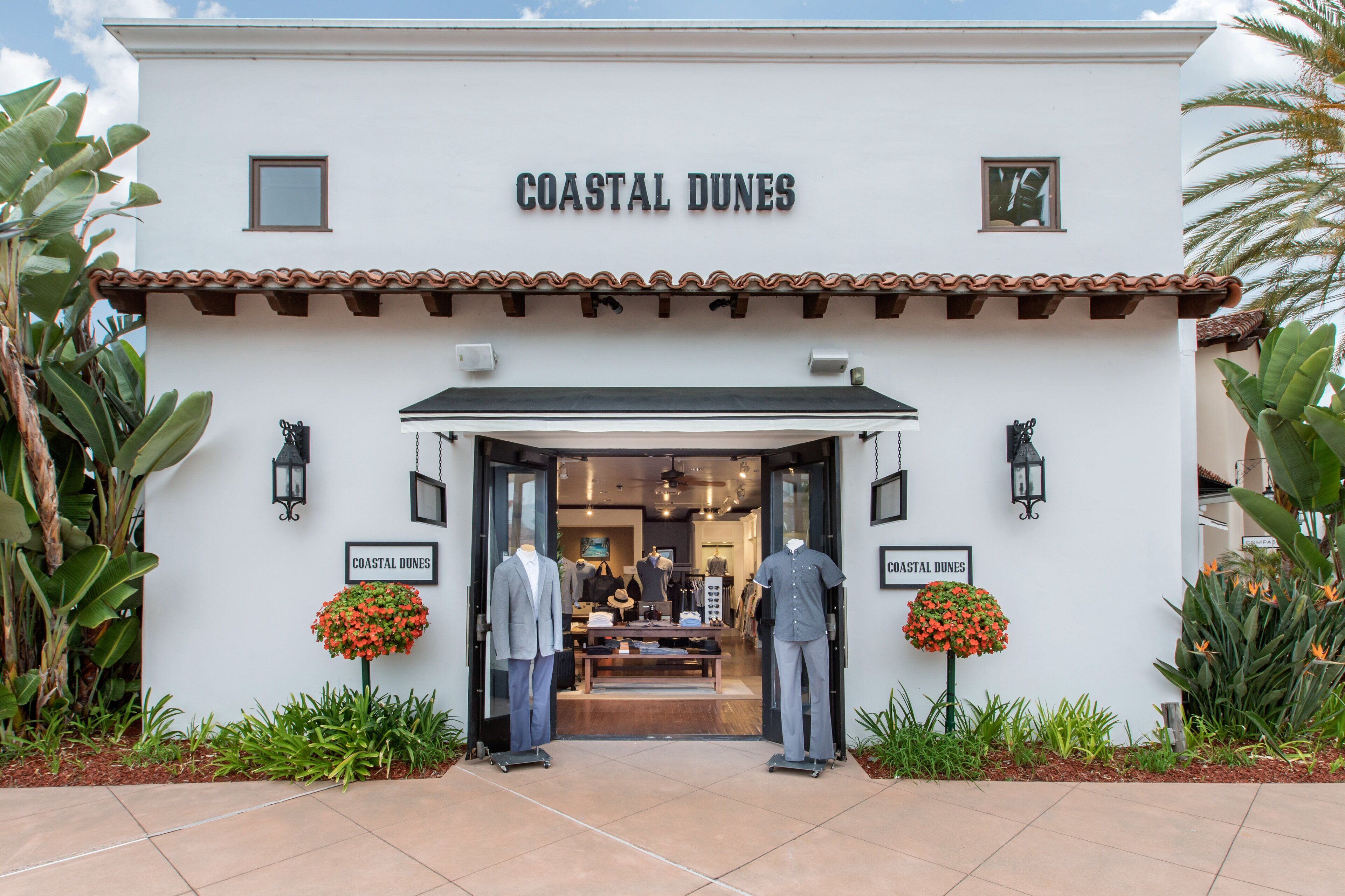 The exterior of Coastal Dunes, featuring a white facade, tiled roof, and two mannequins in front.