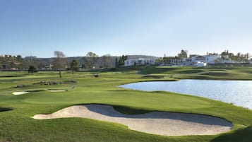Um campo de golfe com bunkers, lago e um clube de campo ao fundo.