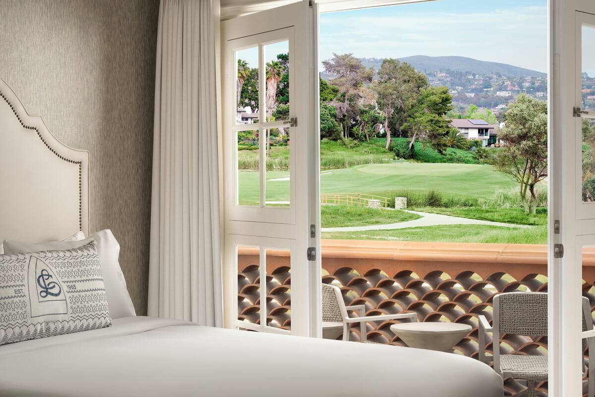 A bedroom with a large bed, a view of a golf course, and a balcony with chairs and a table.