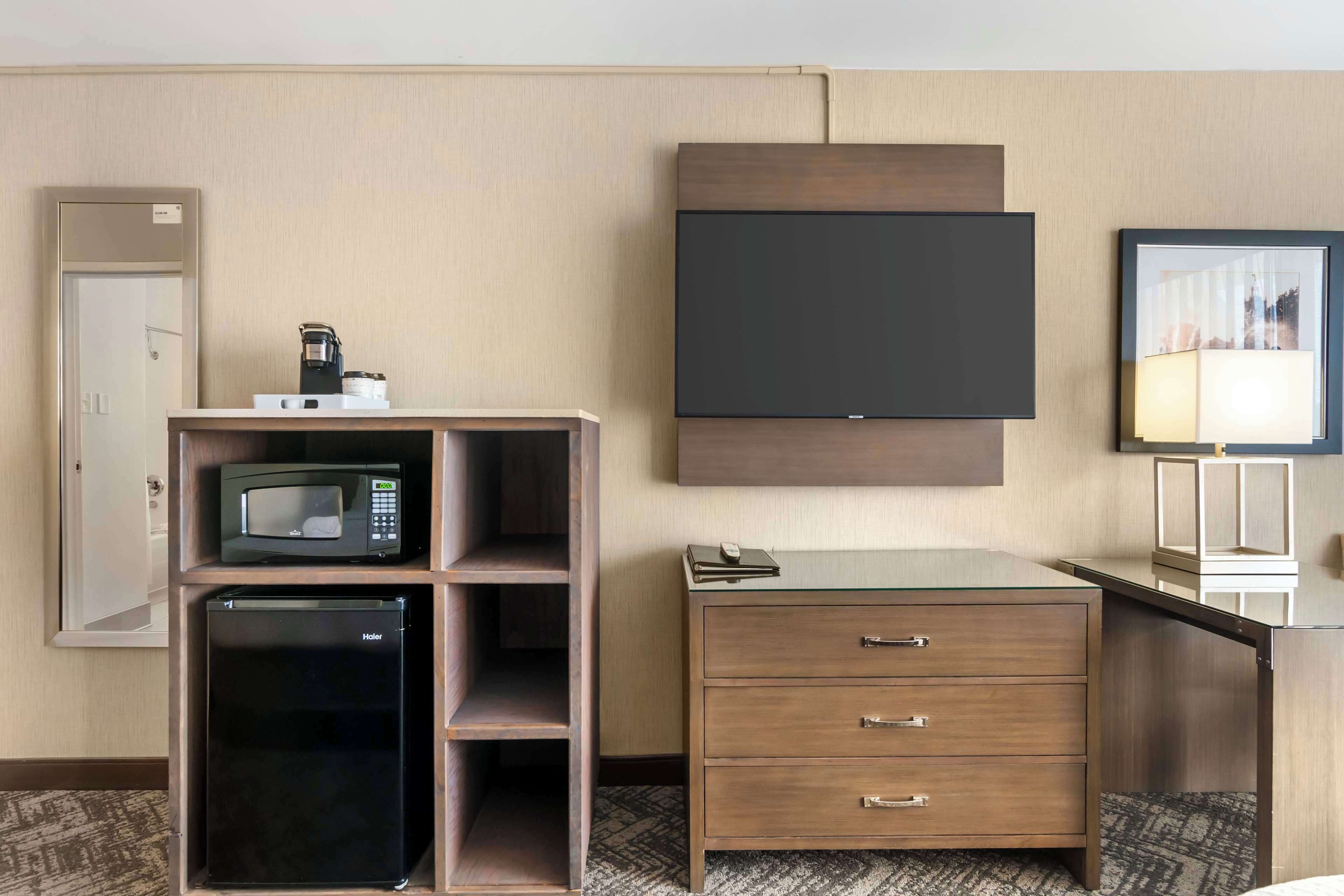 A hotel room with a minibar, a flat-screen TV, a desk with drawers, and a framed picture on the wall.