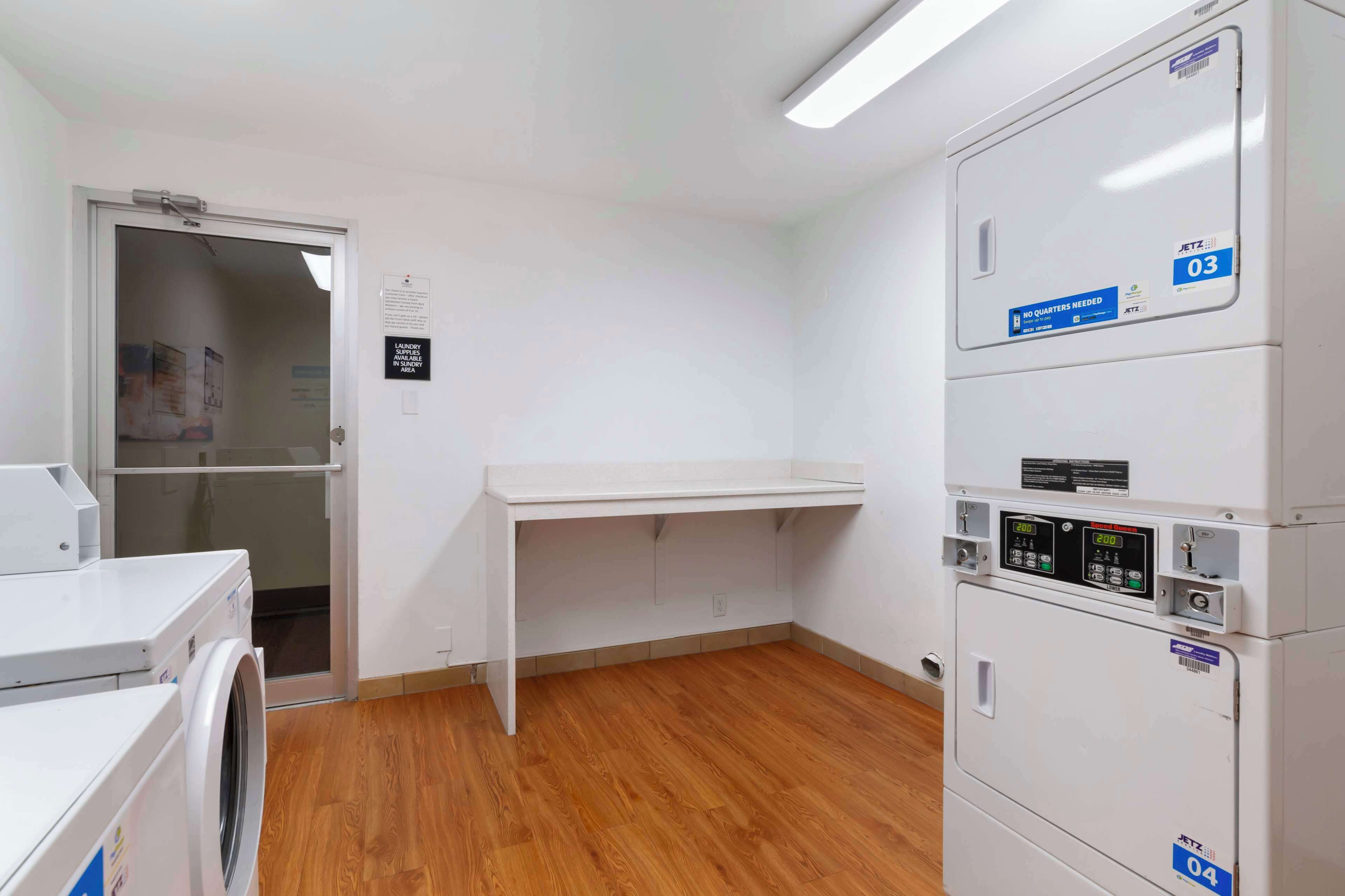 A laundry area with a washing machine, a drying rack, and stacked dryers.