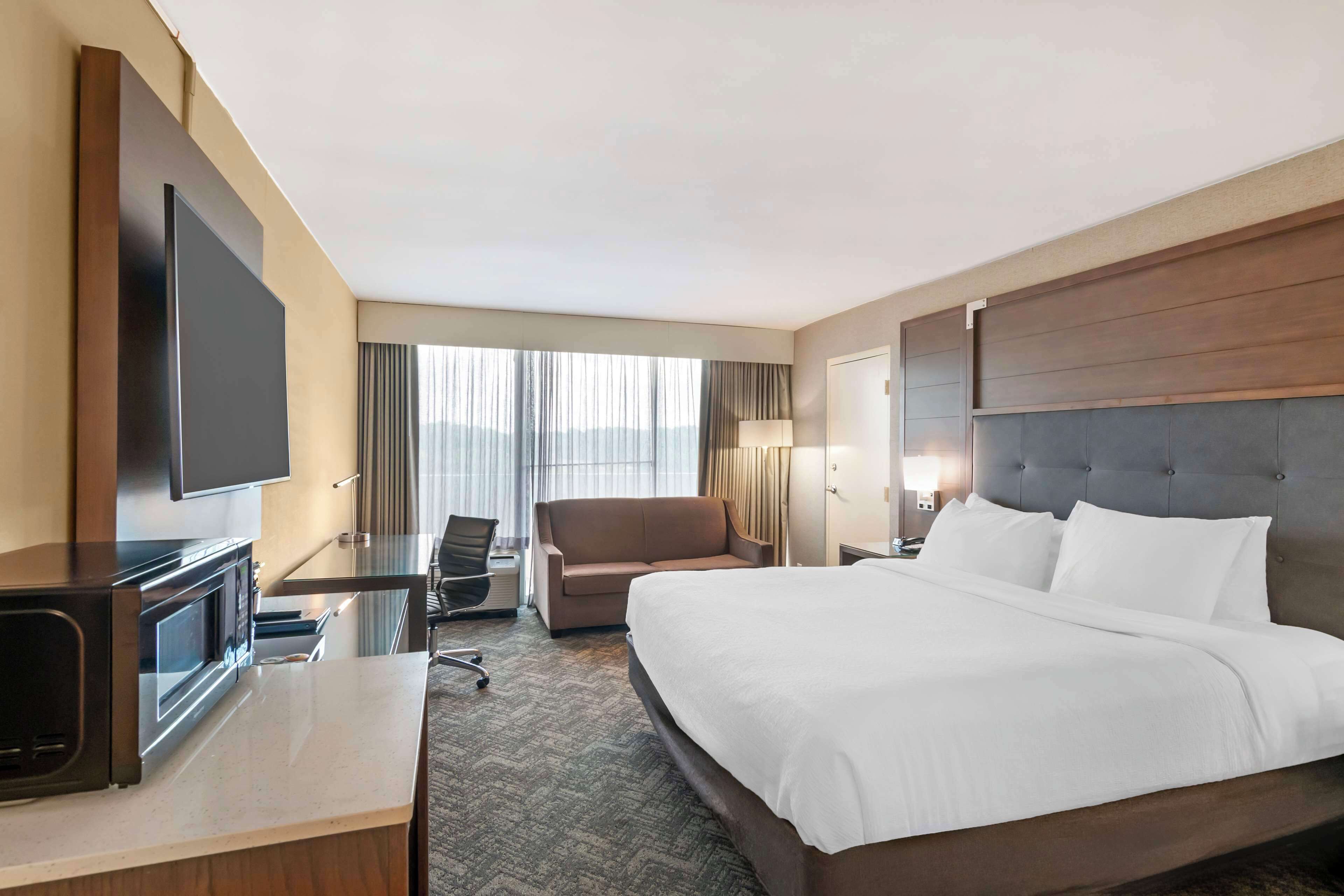 Une chambre d’hôtel avec un grand lit, un téléviseur à écran plat, un bureau avec une chaise et une fenêtre avec des rideaux.