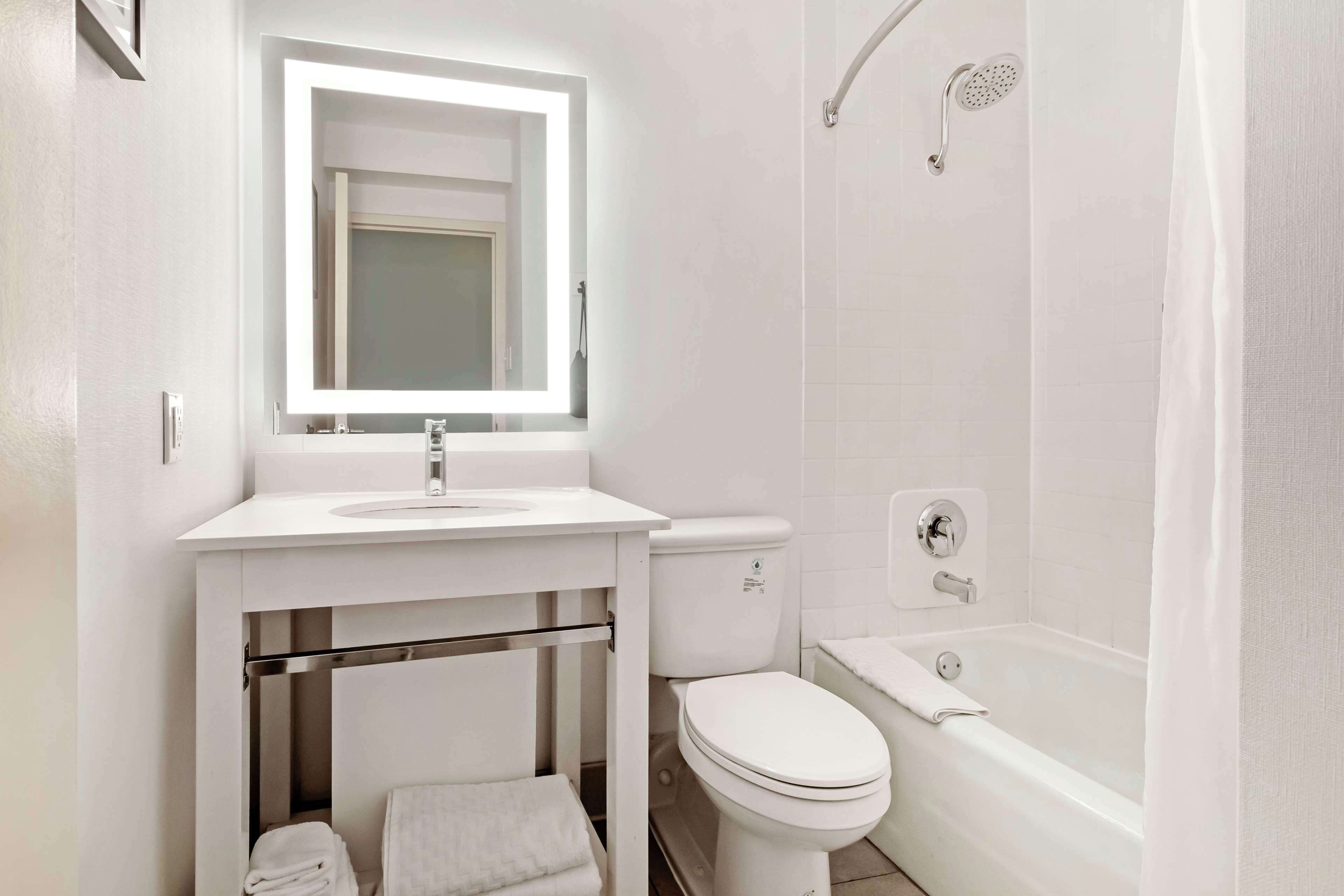 A modern bathroom with a white sink, mirror, toilet, and bathtub.
