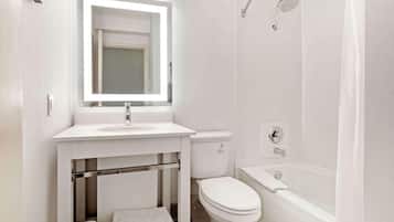 A modern bathroom with a white sink, mirror, toilet, and bathtub.