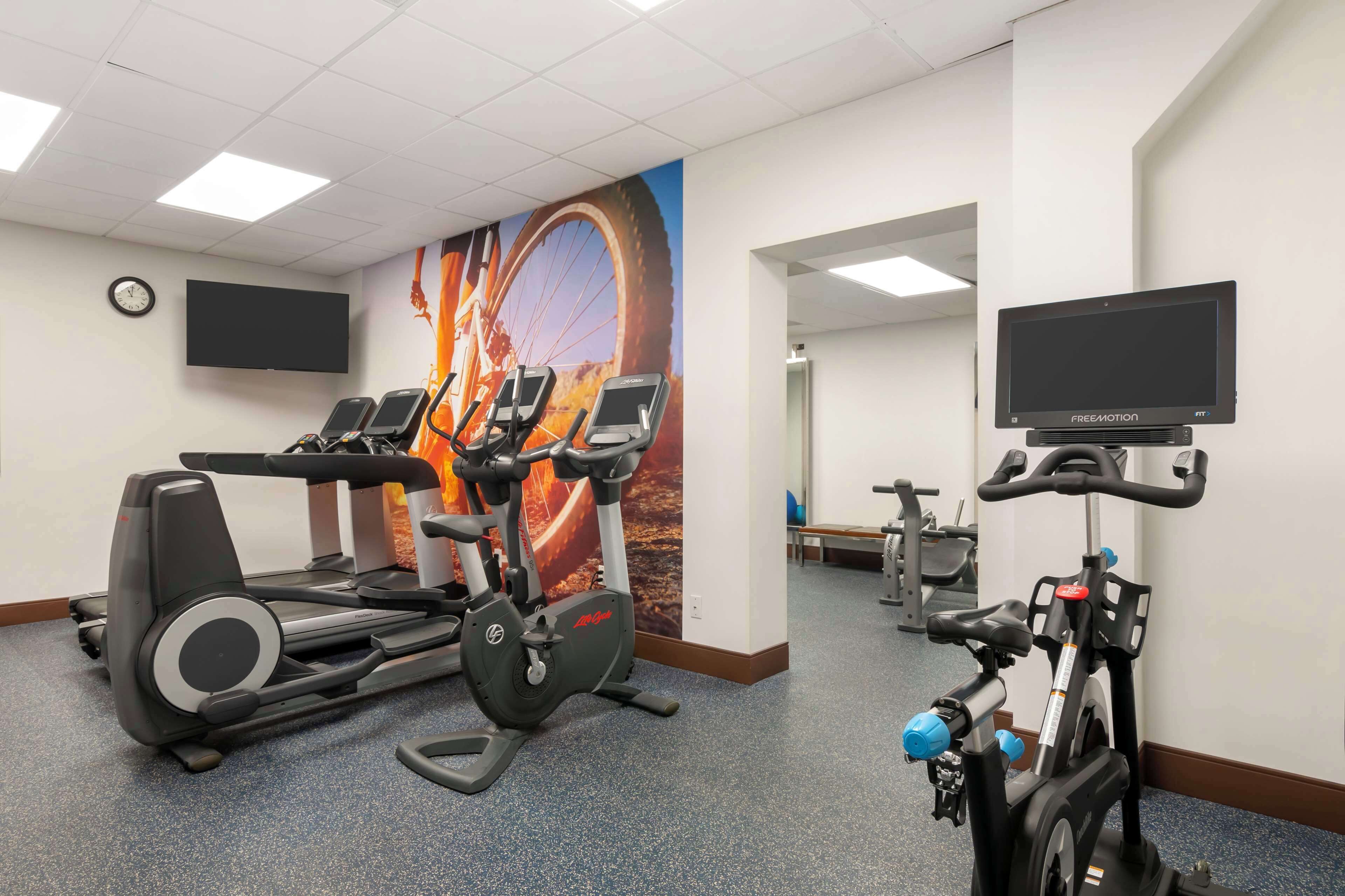 Une salle de sport équipée de vélos d’appartement, de tapis de course et d’un écran de télévision.