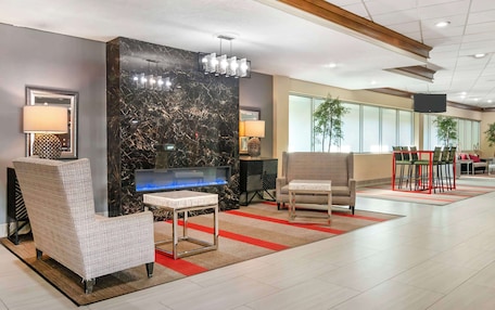 A modern lobby with a marble reception desk, comfortable seating, a flat-screen TV, and a large window providing natural light.