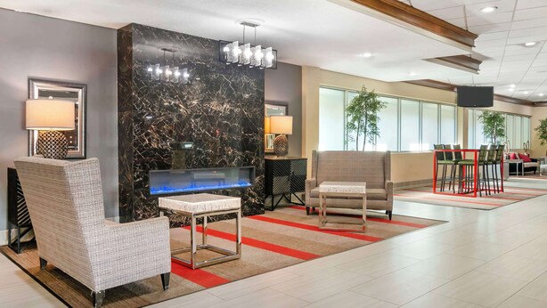 A modern lobby with a marble reception desk, comfortable seating, a flat-screen TV, and a large window providing natural light. - Best Western Plus Kansas City Sports Complex Hotel (Kansas City)