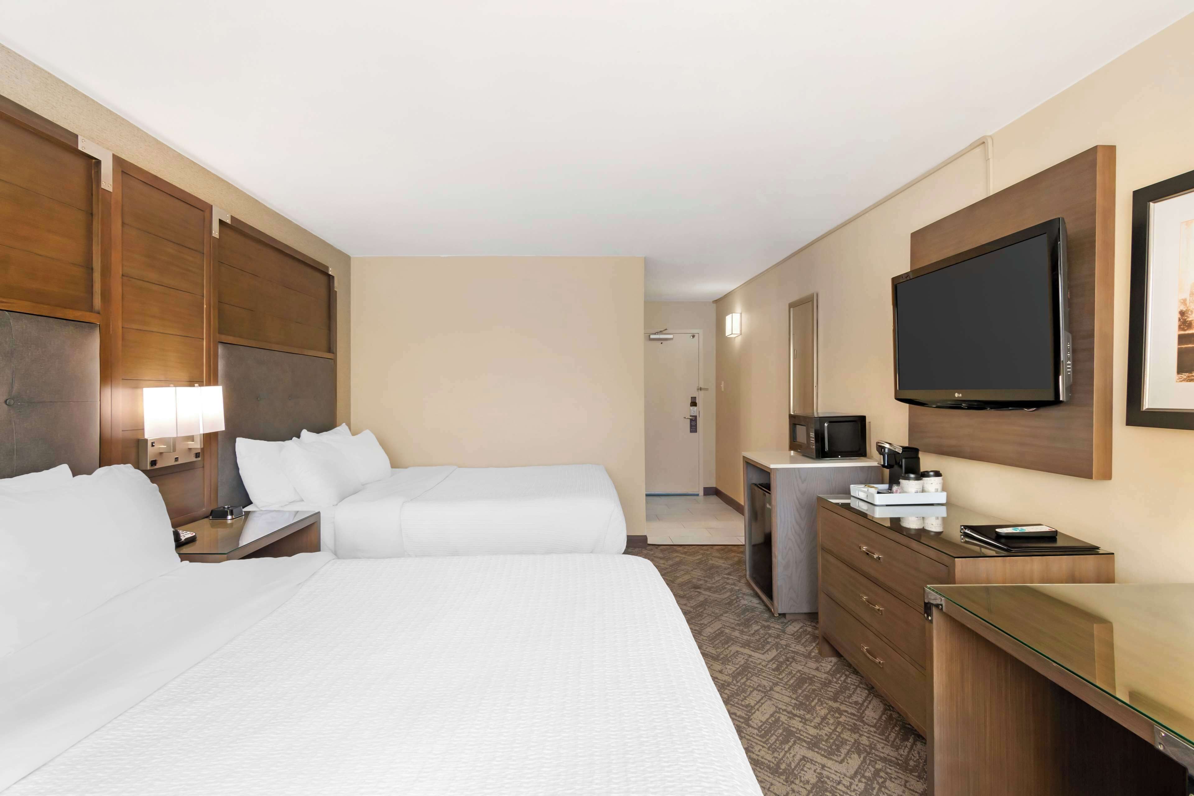 A hotel room with two beds, a desk, a television, and a minibar.