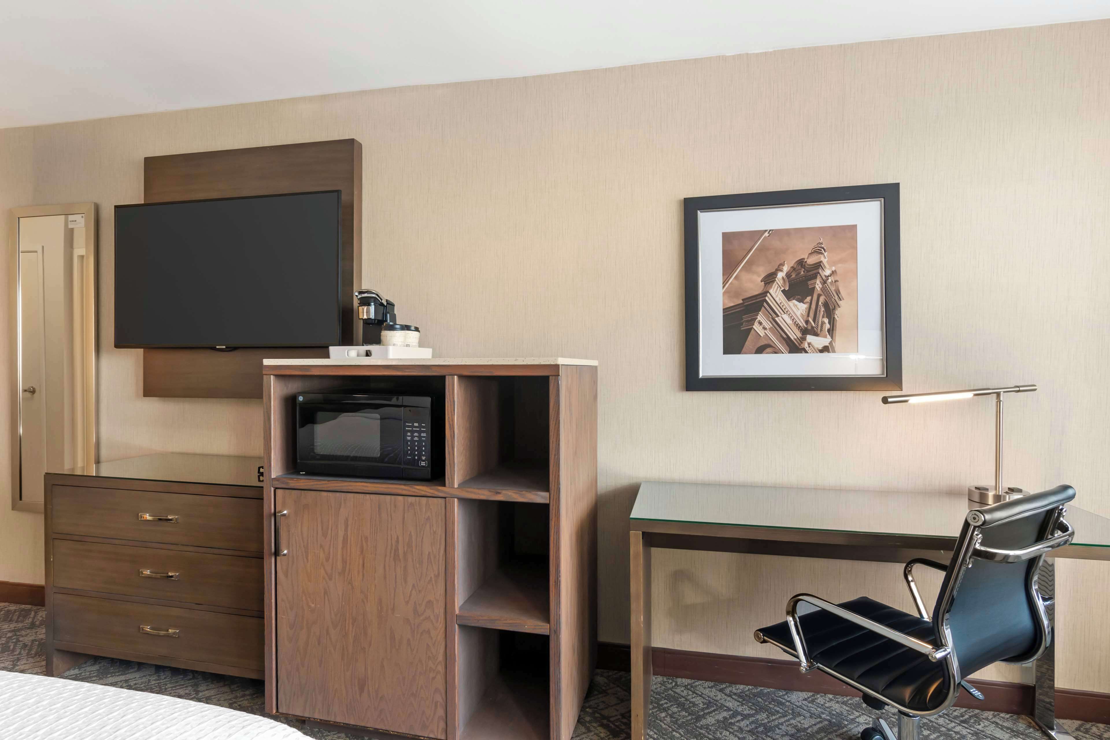 Une chambre d’hôtel équipée d’un téléviseur à écran plat, d’un four à micro-ondes, d’une machine à café, d’un tableau encadré au mur, d’un bureau avec une chaise et d’une armoire.