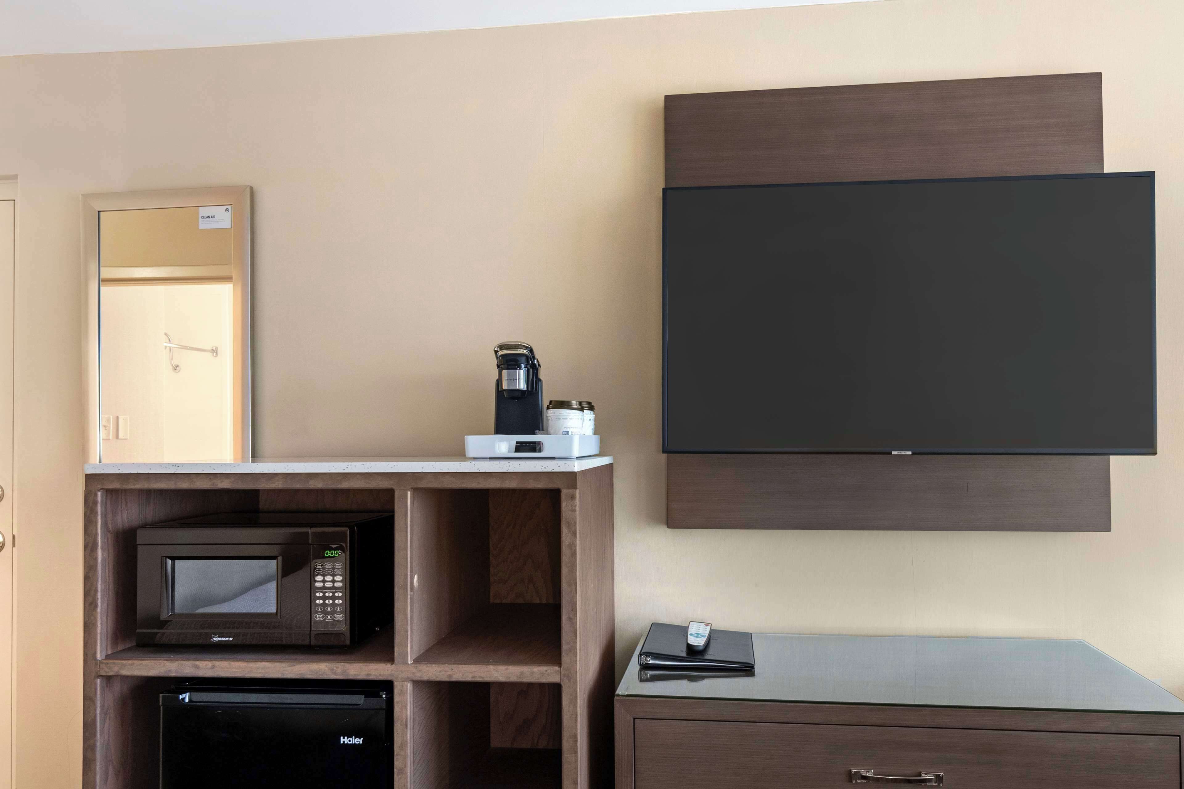 Habitación de hotel con microondas, cafetera y televisor de pantalla plana montado en la pared.