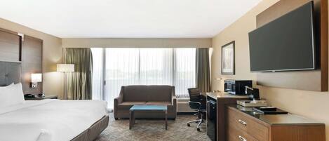 Una habitación de hotel con una cama grande, un escritorio con computadora, una silla y un televisor.