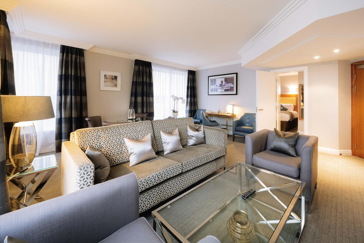 A modern living room with a patterned sofa, a glass coffee table, and a seating area with a chair.