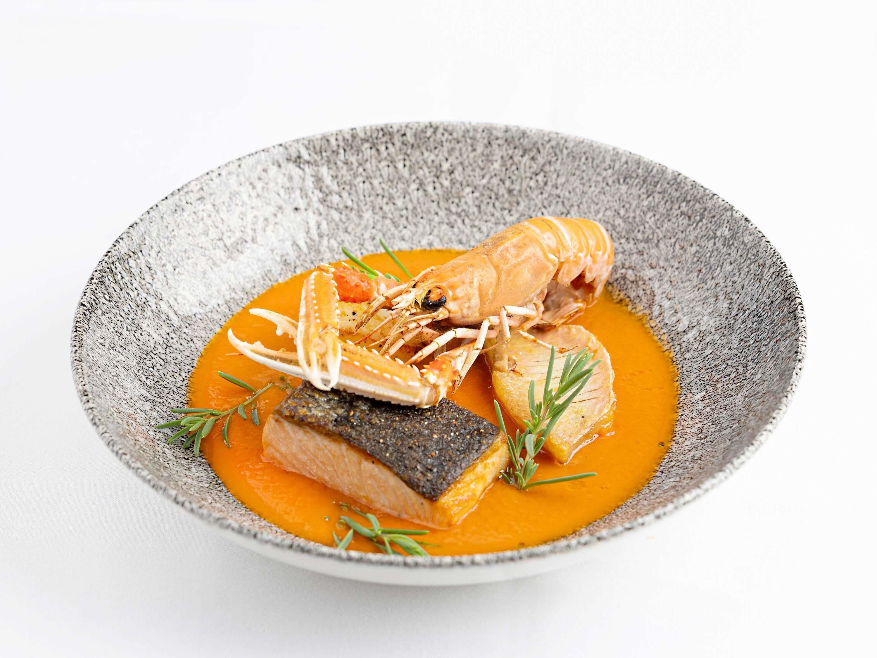 Un plato con salmón, langosta y un trozo de pescado oscuro, adornado con hierbas.