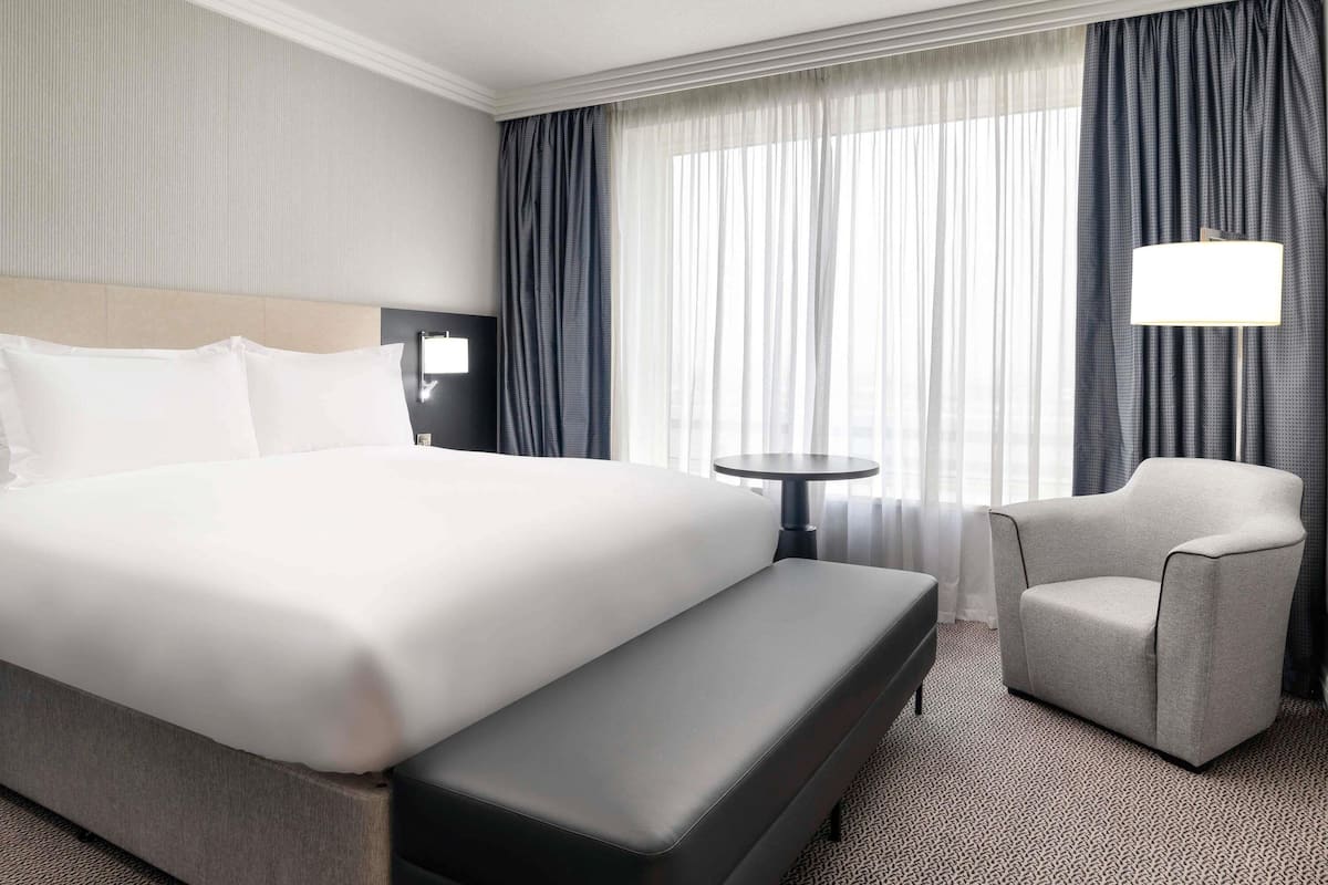 A hotel room with a large bed, a small table, a chair, and a lamp.