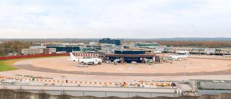 An airport terminal with multiple gates, a large building in the background, and a curved road leading to the terminal.
