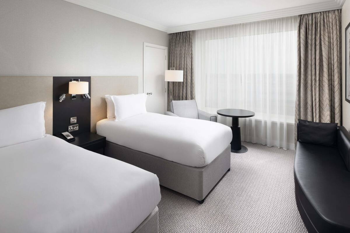 A hotel room with two beds, a desk, a chair, a round table, and a sofa.