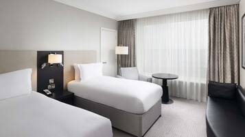 A hotel room with two beds, a desk, a chair, a round table, and a sofa.