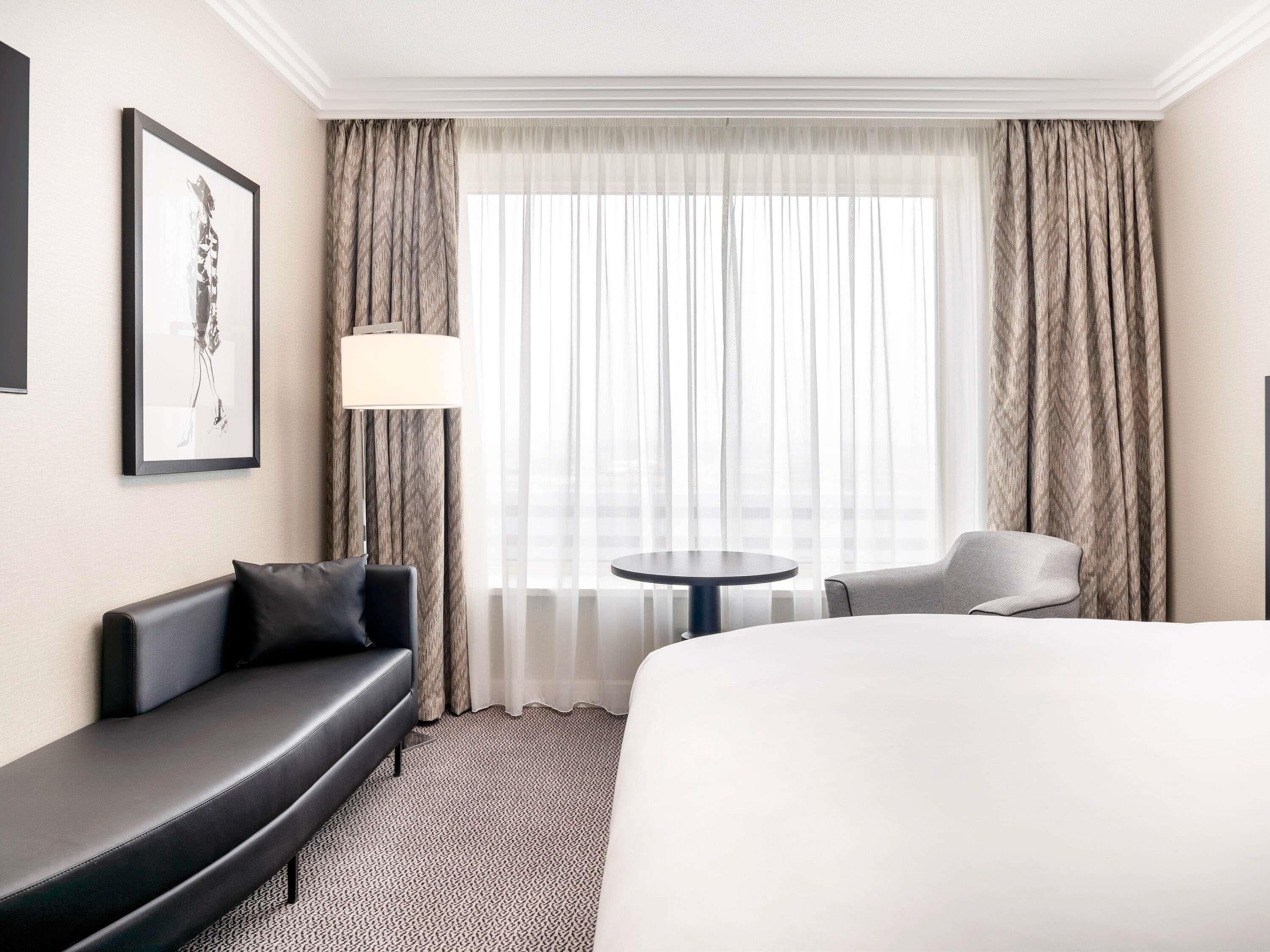 A hotel room with a bed, a sofa, a chair, a small round table, and a lamp.
