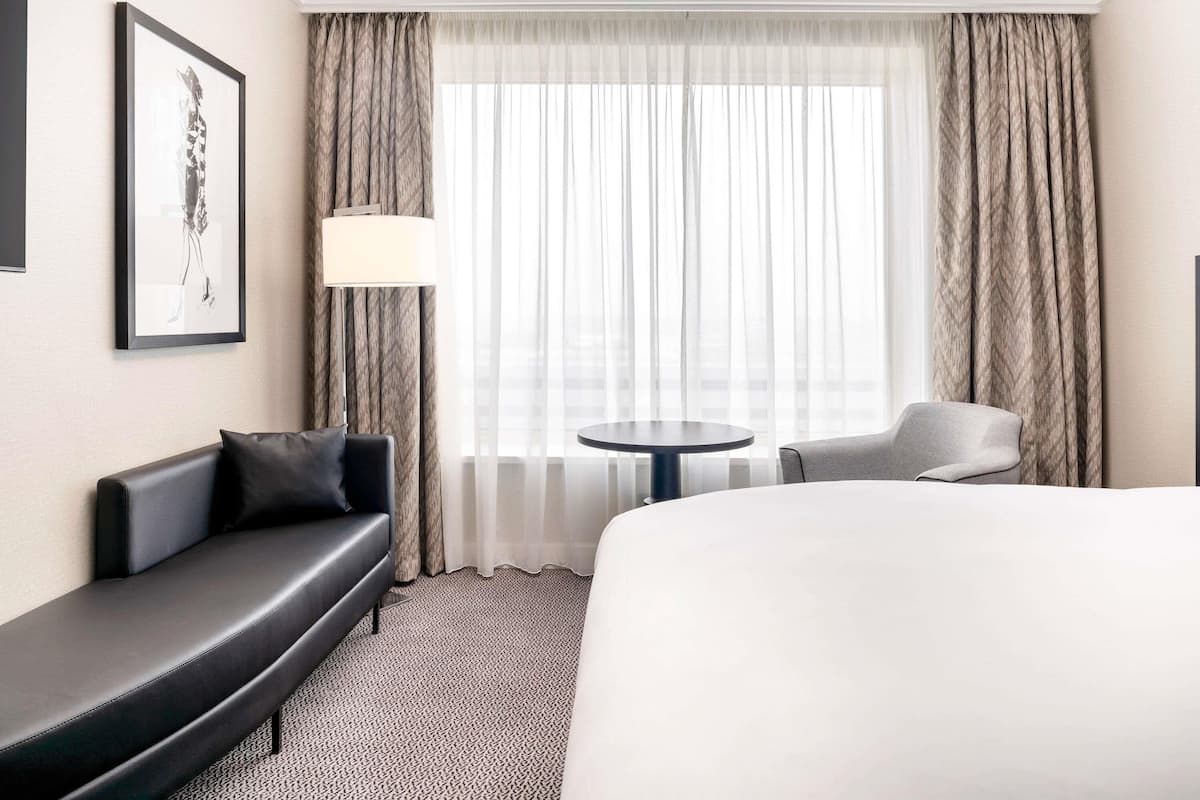 A hotel room with a bed, a sofa, a chair, a small round table, and a lamp.