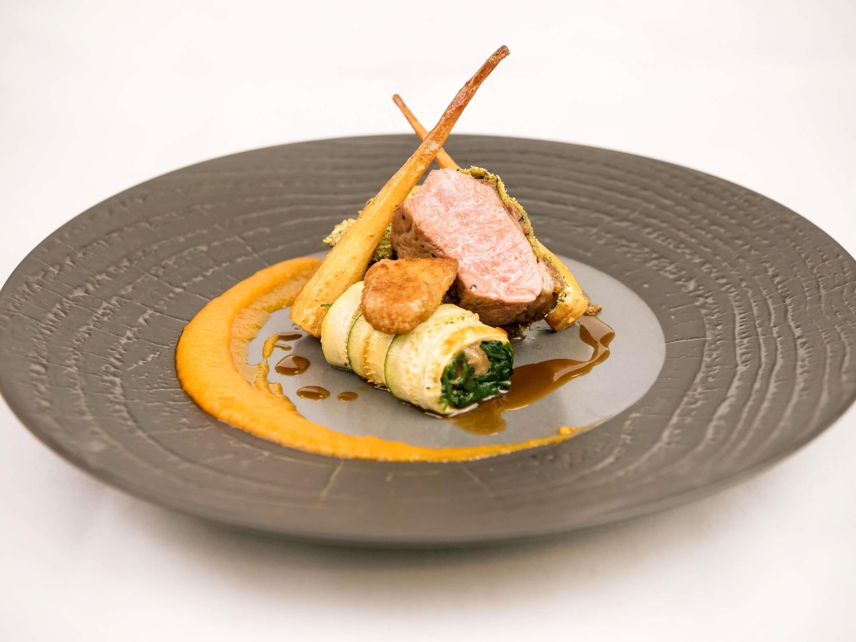 A plate with a dish consisting of meat, vegetables, and a sauce.