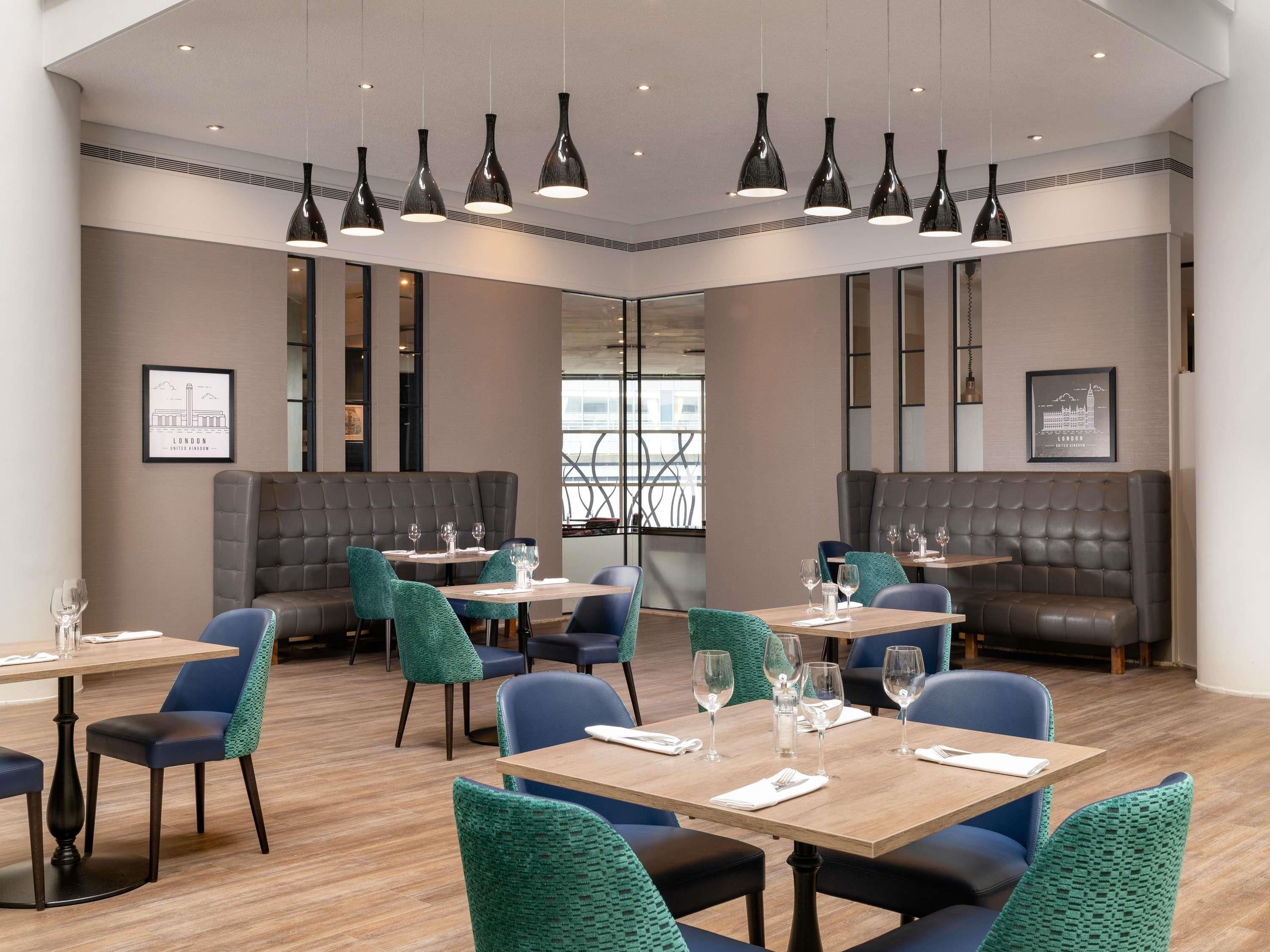 A modern dining area with booths and tables, overhead pendant lighting, and framed cityscape artwork on the walls.