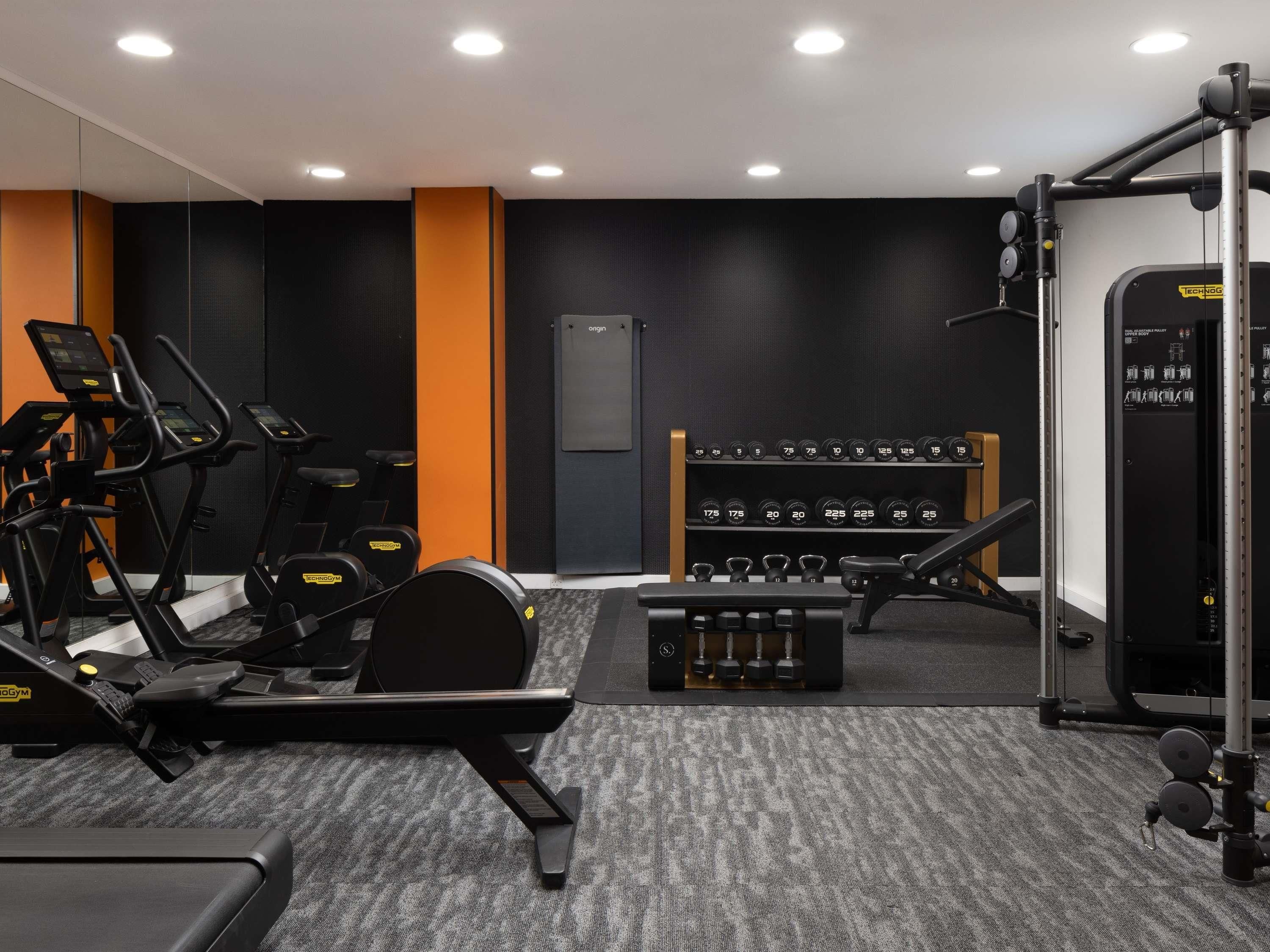 Une salle de sport équipée de tapis de course, de bancs de musculation et d’une série d’haltères.